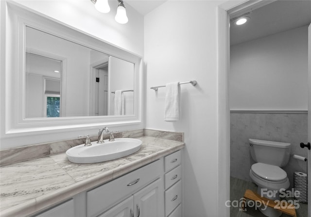 bathroom featuring toilet, vanity, and tile walls