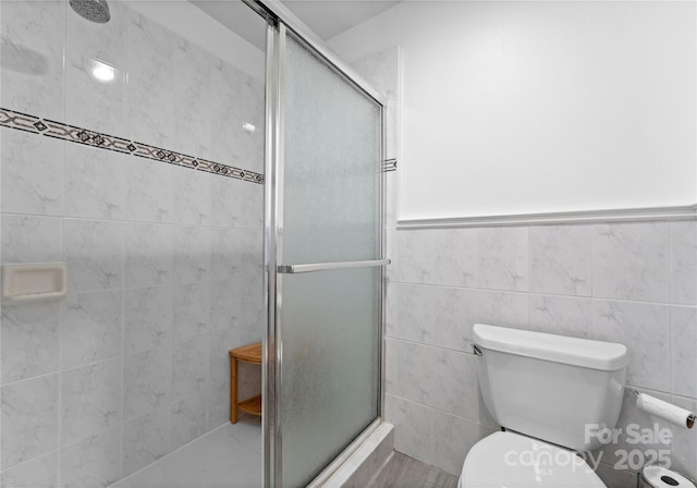 full bath featuring tile walls, a shower stall, toilet, and a wainscoted wall