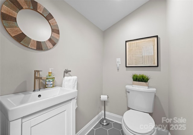 bathroom with baseboards, vaulted ceiling, tile patterned floors, toilet, and vanity