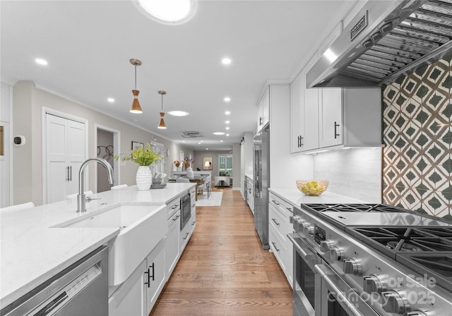 kitchen with high end appliances, under cabinet range hood, recessed lighting, decorative light fixtures, and white cabinetry