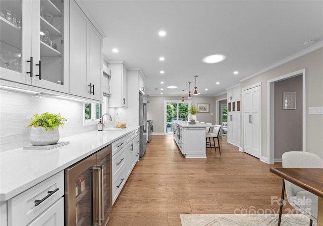 kitchen featuring wine cooler, a sink, ornamental molding, a kitchen breakfast bar, and white cabinets