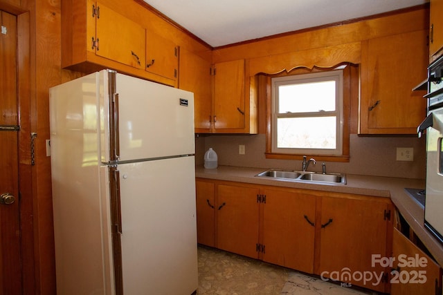kitchen with light countertops, freestanding refrigerator, a sink, and crown molding