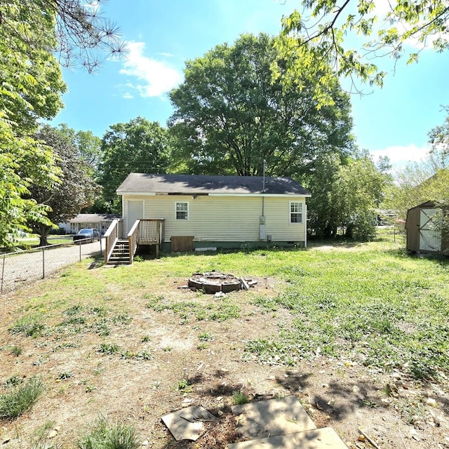rear view of house with a fire pit, a shed, an outbuilding, crawl space, and fence