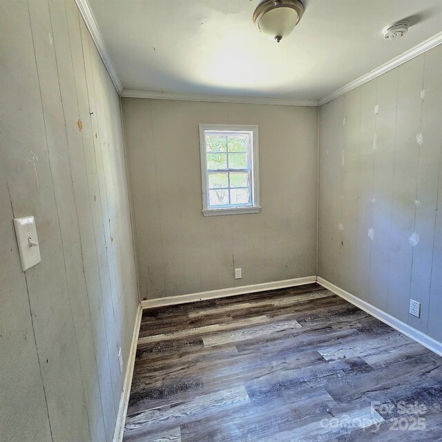 empty room with crown molding, wood walls, and wood finished floors