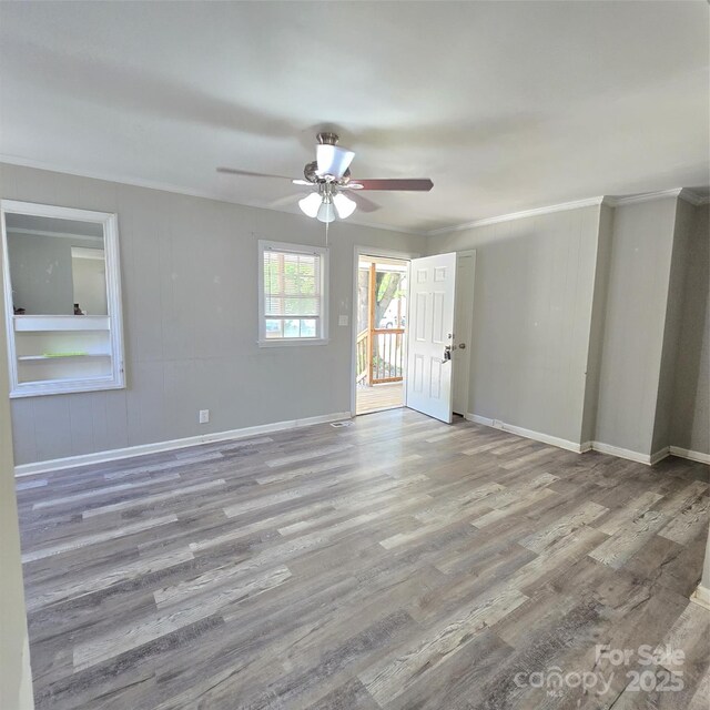 empty room featuring wood finished floors, a ceiling fan, ornamental molding, and baseboards
