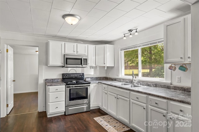 kitchen with appliances with stainless steel finishes, a sink, white cabinets, and dark countertops