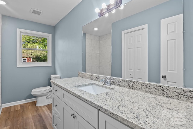 full bath featuring baseboards, wood finished floors, toilet, vanity, and tiled shower