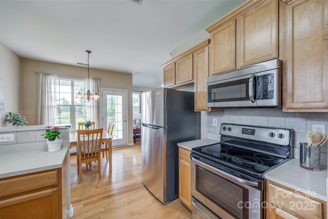 kitchen featuring light wood-type flooring, light countertops, decorative backsplash, and appliances with stainless steel finishes
