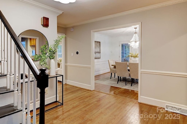 foyer entrance featuring ornamental molding, arched walkways, light wood-style flooring, a notable chandelier, and visible vents