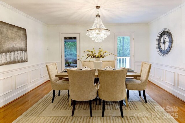 dining space with light wood-type flooring, a decorative wall, plenty of natural light, and an inviting chandelier