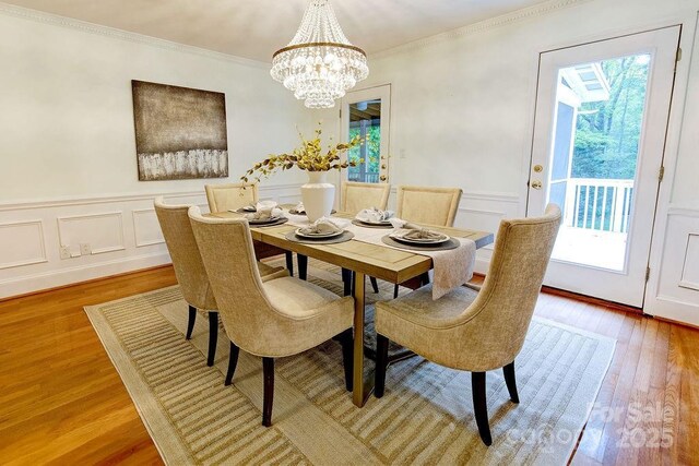 dining room with wood finished floors, crown molding, a wainscoted wall, and an inviting chandelier