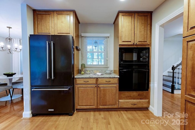 kitchen with an inviting chandelier, light wood-type flooring, brown cabinetry, and black appliances