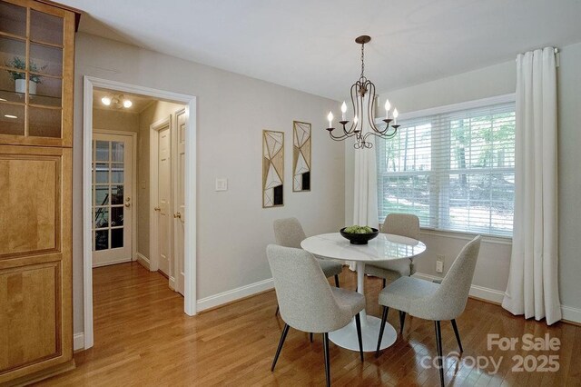 dining area with light wood finished floors, baseboards, and an inviting chandelier