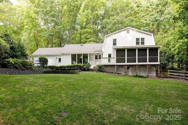 rear view of house with a gambrel roof, a chimney, fence, a yard, and a sunroom