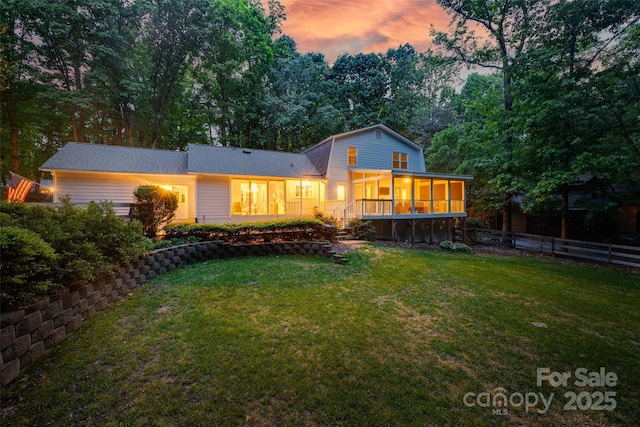 rear view of property featuring a yard, a sunroom, a gambrel roof, and fence