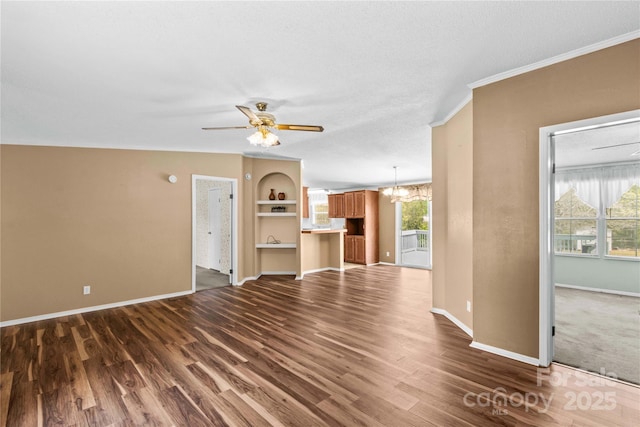 unfurnished living room with crown molding, baseboards, dark wood-style flooring, and ceiling fan with notable chandelier