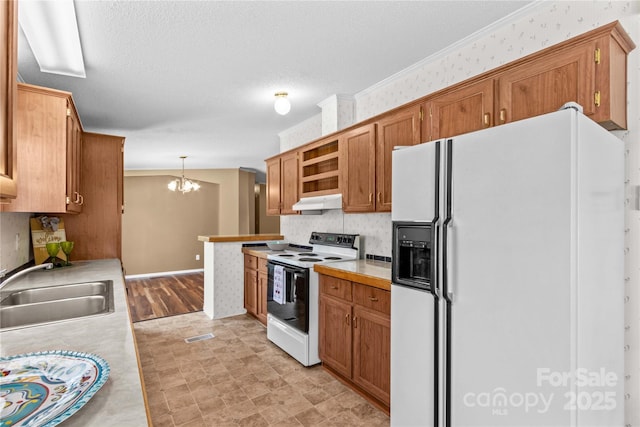 kitchen featuring under cabinet range hood, light countertops, a sink, white appliances, and a notable chandelier