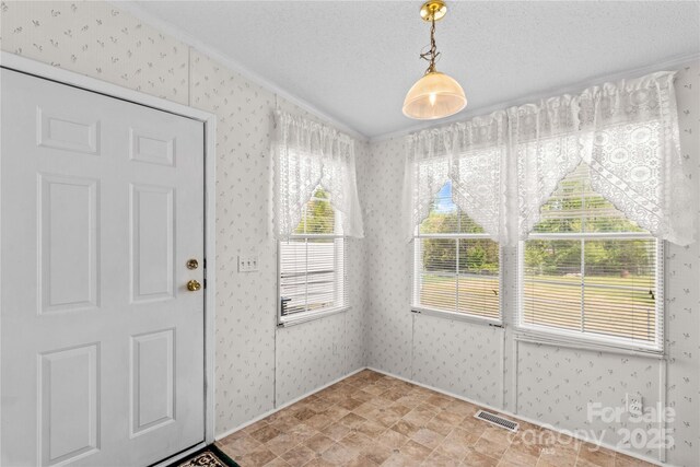unfurnished dining area featuring crown molding, visible vents, a textured ceiling, and wallpapered walls