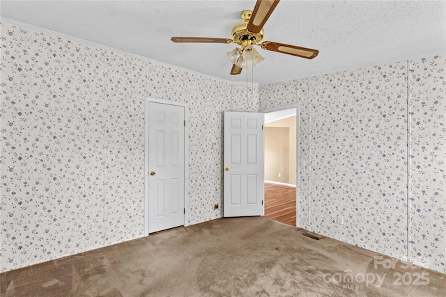 unfurnished bedroom featuring crown molding, wallpapered walls, ceiling fan, carpet flooring, and visible vents