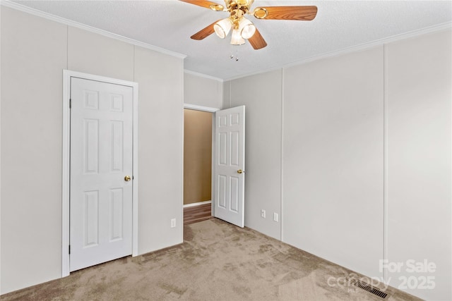 unfurnished bedroom featuring carpet, visible vents, crown molding, and a ceiling fan