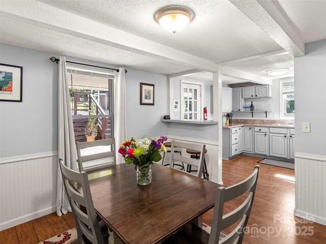 dining area with light wood finished floors, a textured ceiling, wainscoting, and beam ceiling