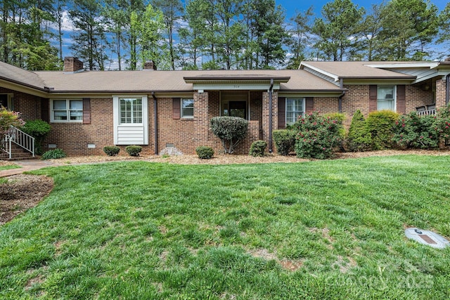 ranch-style home with a chimney, a shingled roof, a front yard, and brick siding