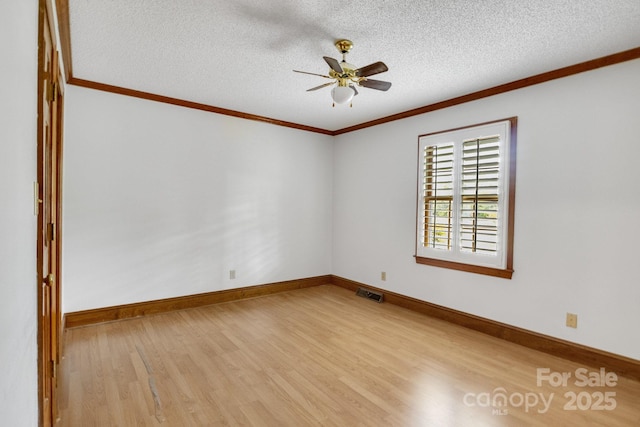 empty room with baseboards, ornamental molding, visible vents, ceiling fan, and wood finished floors