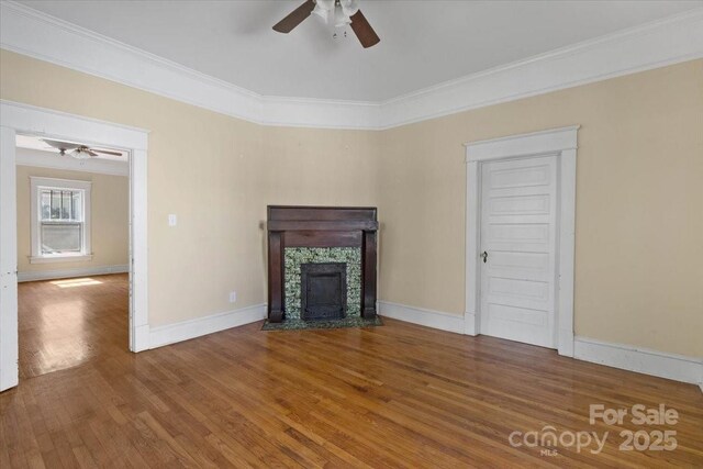 unfurnished living room featuring a tiled fireplace, wood finished floors, ornamental molding, and ceiling fan