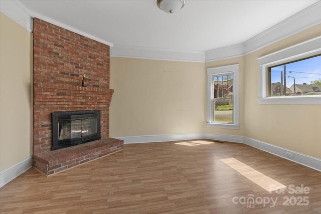 unfurnished living room featuring wood finished floors, a brick fireplace, baseboards, and ornamental molding
