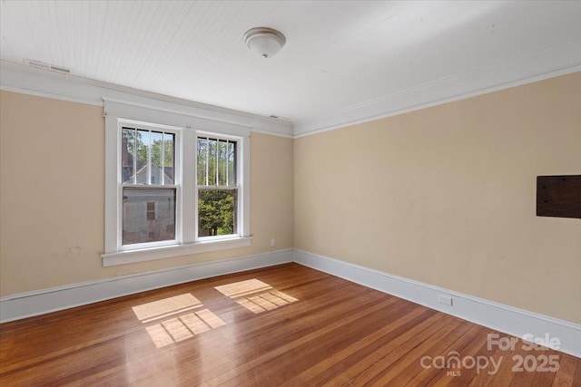 unfurnished room with wood finished floors, visible vents, baseboards, and ornamental molding