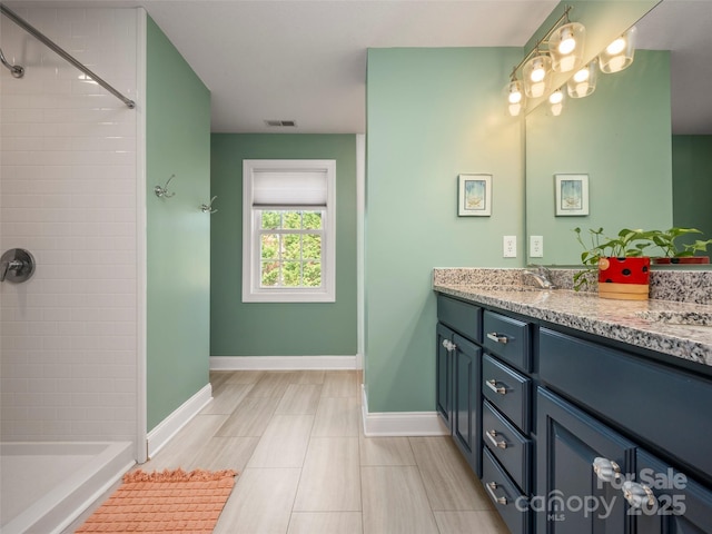 bathroom with baseboards, tiled shower, and vanity