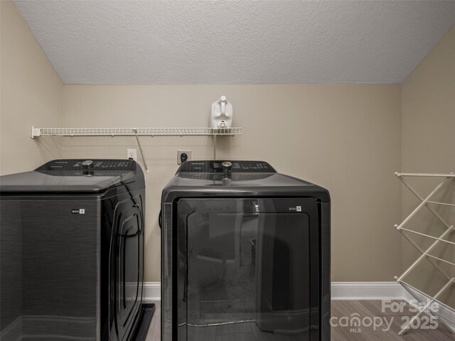 clothes washing area with laundry area, a textured ceiling, wood finished floors, washer and dryer, and baseboards