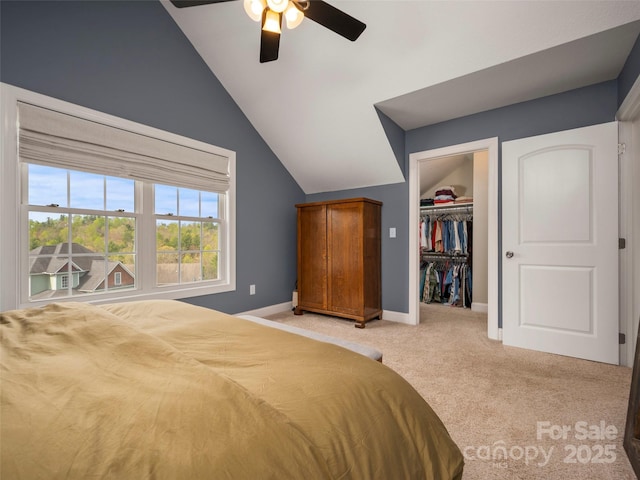 bedroom featuring a ceiling fan, a spacious closet, vaulted ceiling, light carpet, and baseboards