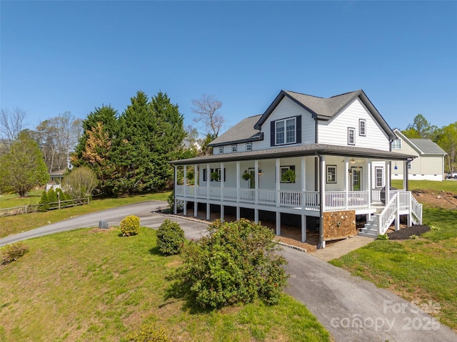 farmhouse inspired home with roof with shingles, a porch, a front lawn, and aphalt driveway