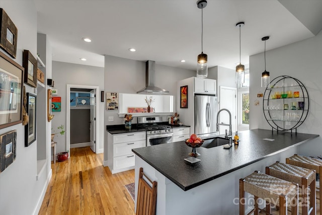 kitchen with wall chimney exhaust hood, white cabinets, dark countertops, a breakfast bar, and appliances with stainless steel finishes