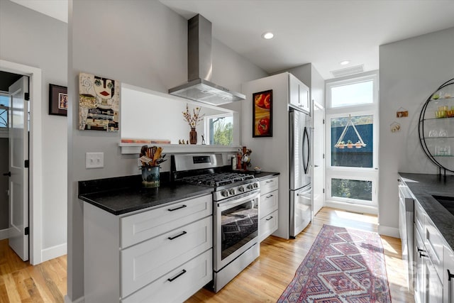 kitchen with dark countertops, wall chimney exhaust hood, appliances with stainless steel finishes, and a wealth of natural light