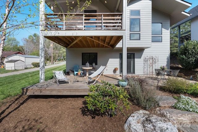 back of property featuring a wooden deck, a lawn, and a balcony
