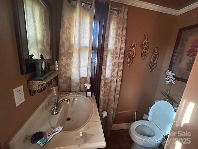 bathroom featuring baseboards, a sink, crown molding, and toilet