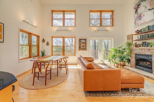 living room featuring a high ceiling, a stone fireplace, french doors, baseboards, and light wood-style flooring