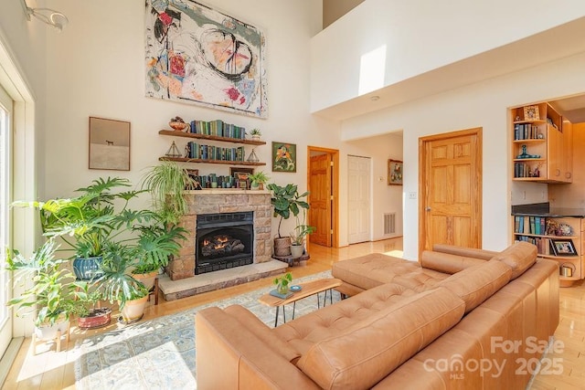 living room featuring light wood-type flooring, a stone fireplace, visible vents, and a high ceiling