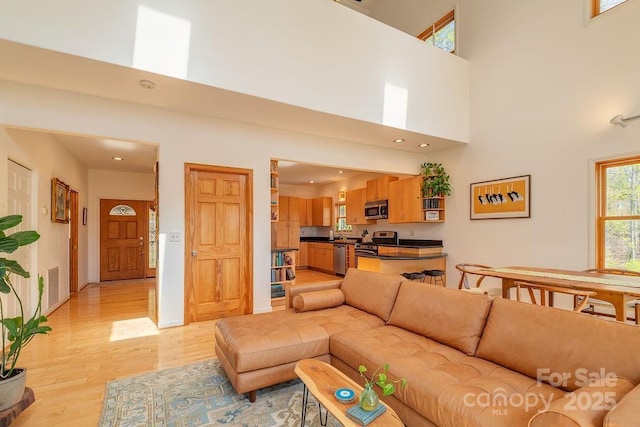 living area featuring recessed lighting, a high ceiling, light wood finished floors, visible vents, and baseboards