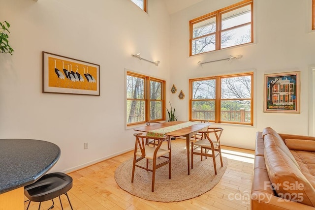 dining space featuring light wood-type flooring, baseboards, and a high ceiling