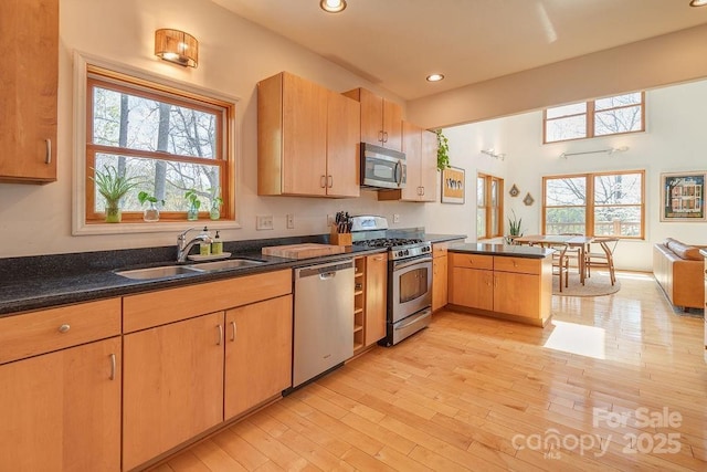 kitchen with a sink, stainless steel appliances, light wood finished floors, a peninsula, and recessed lighting