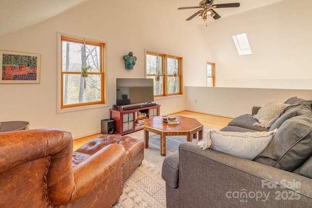 living room featuring a ceiling fan, baseboards, light wood-style flooring, and vaulted ceiling with skylight