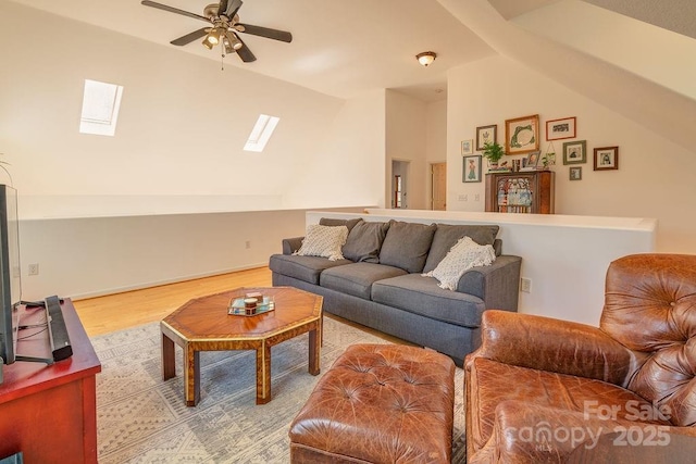 living area with ceiling fan, vaulted ceiling with skylight, and wood finished floors