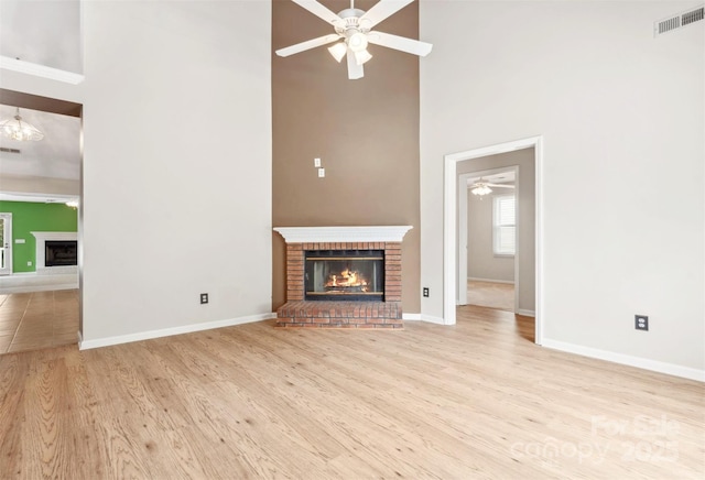 unfurnished living room featuring ceiling fan, a high ceiling, a fireplace, wood finished floors, and visible vents