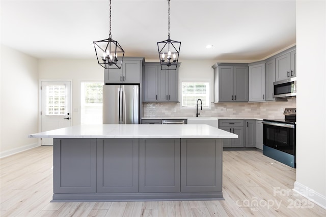 kitchen featuring a sink, stainless steel appliances, a notable chandelier, gray cabinets, and light countertops