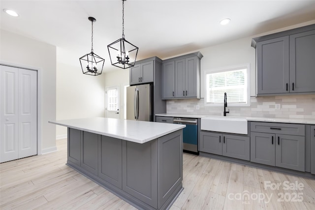 kitchen featuring a sink, freestanding refrigerator, dishwasher, decorative backsplash, and gray cabinetry