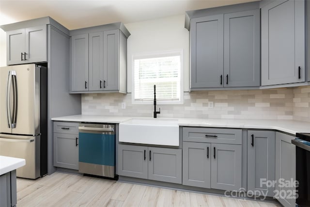 kitchen featuring freestanding refrigerator, gray cabinetry, dishwashing machine, and a sink