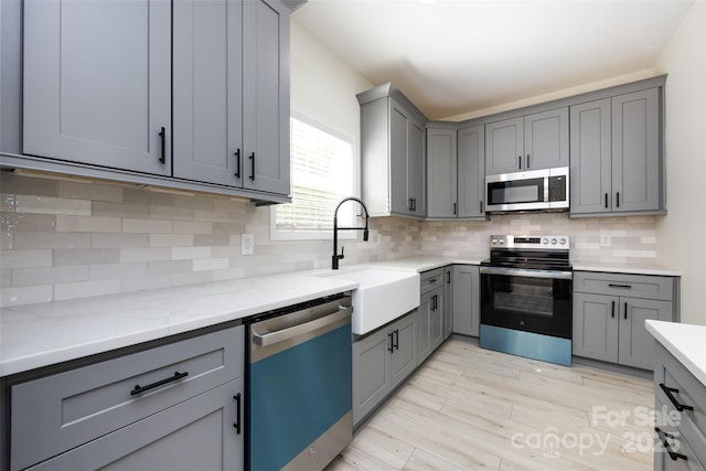 kitchen featuring a sink, tasteful backsplash, gray cabinets, and appliances with stainless steel finishes